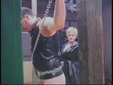 Two dominatrixes inflict pleasurable pain on restrained male slave in a dungeon